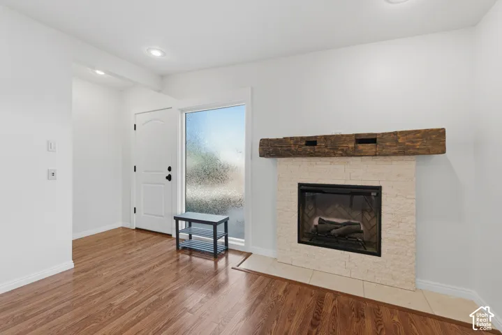 Fireplace featuring a light-toned stone surround, a prominent timber mantel, wood-finish flooring, and recessed ceiling lighting