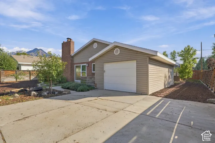 Exterior featuring horizontal siding, a brick chimney, a single-car garage, and concrete driveway with mulch landscaping