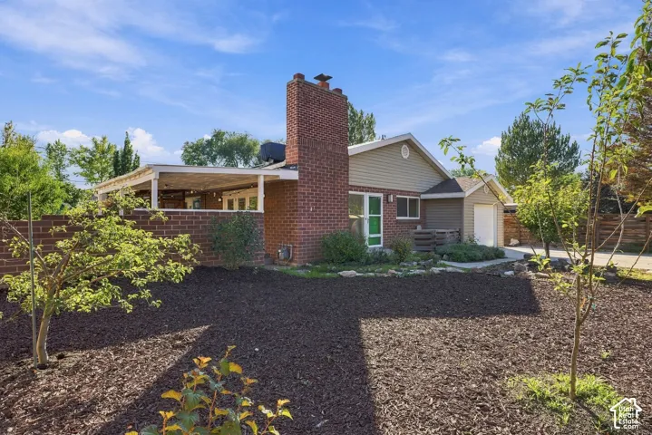 Exterior featuring a brick chimney, a covered patio with a white support structure, a combination of brick and horizontal siding, and a fenced yard with mulched landscape beds