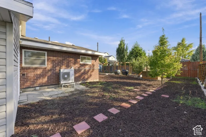 Exterior red brick facade featuring a stone paver walkway, mulch landscaping, mature trees, and wooden perimeter fencing