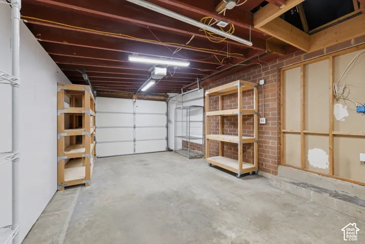 Garage featuring a concrete floor, exposed ceiling joists, brick wall, and overhead lighting
