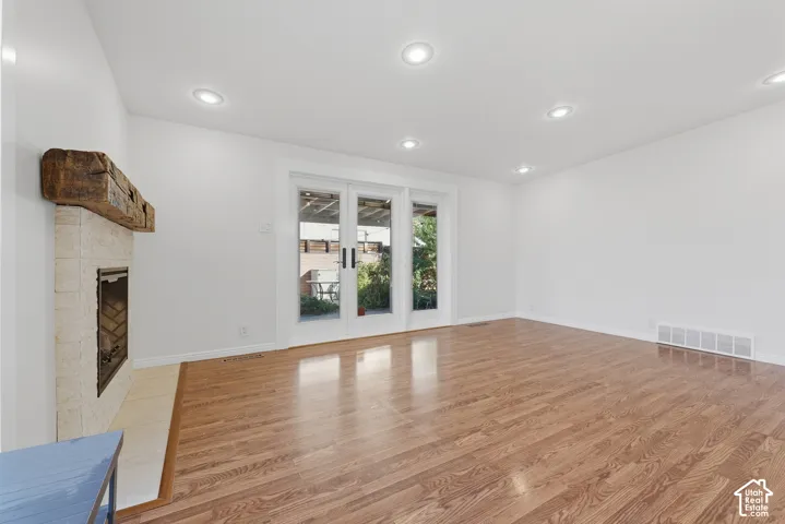 Wood-finish flooring, fireplace with stone surround and reclaimed timber mantel, and double-glass paneled doors featuring recessed lighting