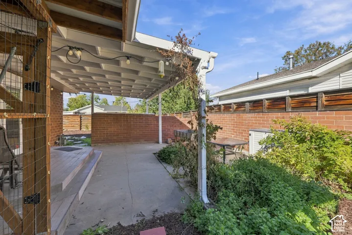Covered concrete patio with a coffered ceiling, perimeter brick masonry walls, and tiered wood-finish decking