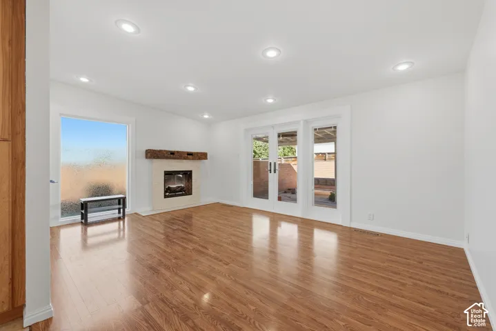 Wood-finish flooring, recessed lighting, fireplace with a stone-texture surround and timber mantel, and glass double doors