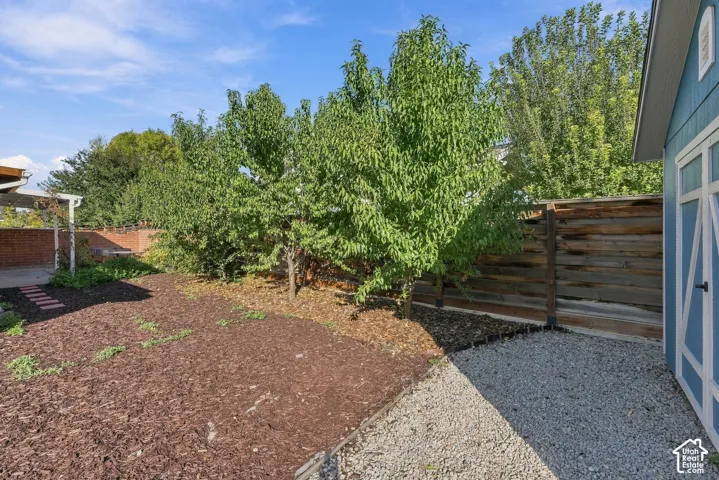 Backyard featuring a wood privacy fence, gravel and mulch ground cover, mature trees, and a detached storage structure