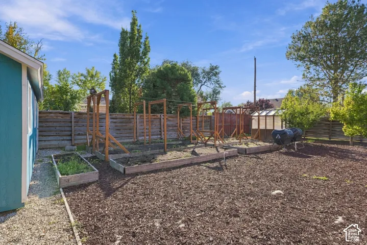 Backyard featuring raised garden beds, wood trellis structures, a greenhouse, and perimeter wood fencing