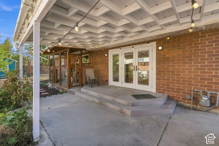 Covered patio featuring a wood-beam pergola, concrete flooring, exterior brick masonry, and multi-lite French doors