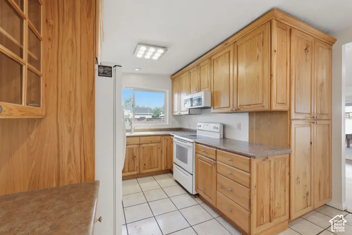 Kitchen featuring natural-finish wood cabinetry, floor-to-ceiling pantry storage, ceramic tile flooring, and laminate countertops