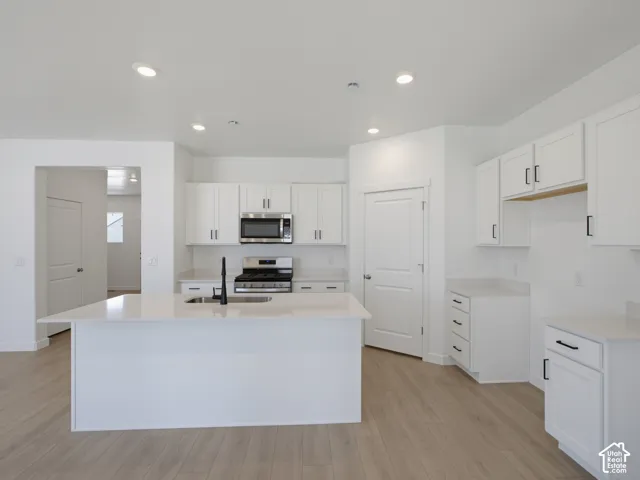 Kitchen featuring white cabinetry, quartz countertops, a central island with an undermount sink, stainless steel appliances, and wood-finish flooring
