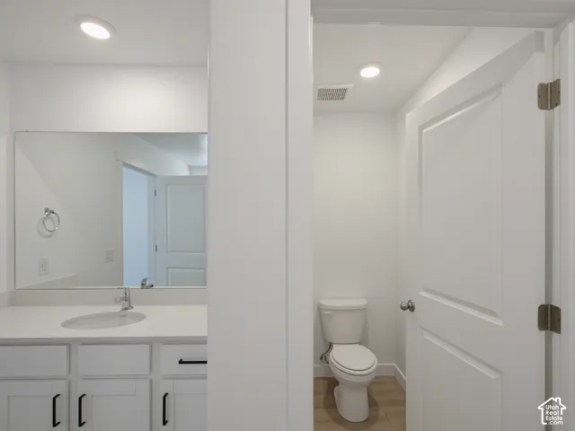 Shaker-style white cabinetry with matte black hardware, integrated rectangular sink, large wall-mounted mirror, wood-finish flooring, and recessed lighting