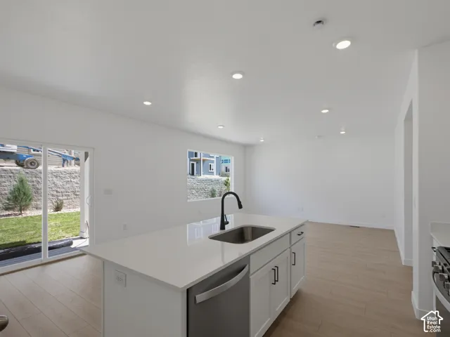 Kitchen featuring a central island with a solid-surface countertop, stainless steel undermount sink, matte black gooseneck faucet, white shaker-style cabinetry, and wood-finish flooring