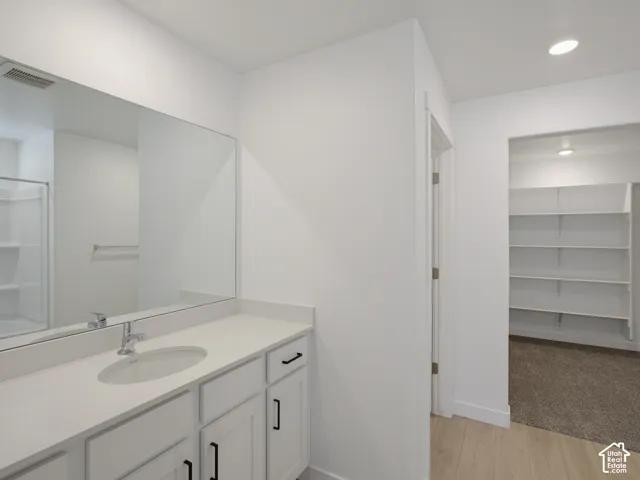 White vanity with an integrated sink and light-toned countertop, large rectangular wall mirror, built-in recessed shelving, and wood-finish flooring