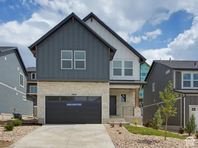 Two-story exterior featuring vertical board-and-batten siding, stone veneer masonry, a multi-paneled garage door, and a covered entryway with a wooden post