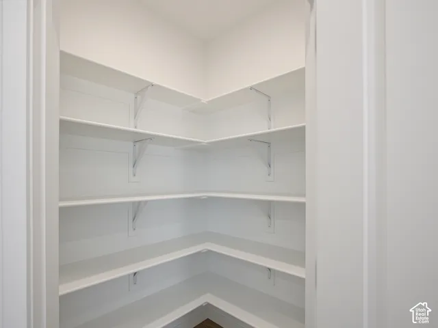 Corner storage space featuring four tiers of white shelving supported by metal brackets