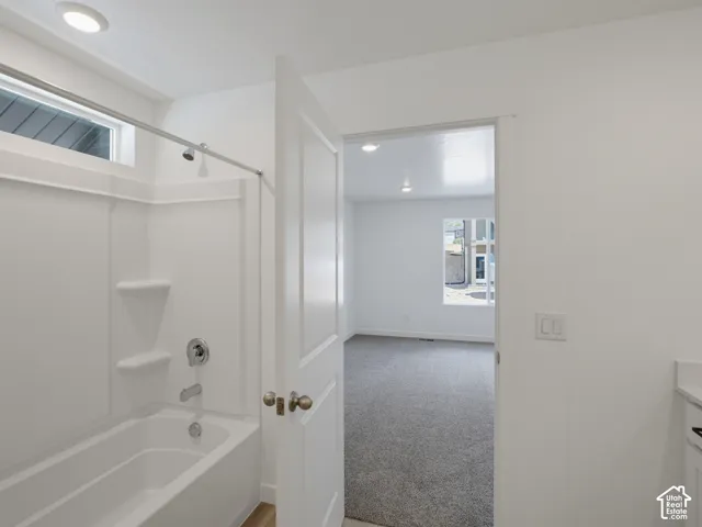 Full-height shower and tub surround with integrated shelving, chrome fixtures, recessed lighting, and neutral carpeting