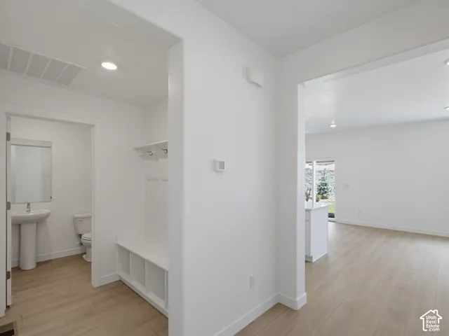 Built-in mudroom bench with integrated shelving and coat hooks, wood-finish flooring, recessed lighting, and a pedestal sink