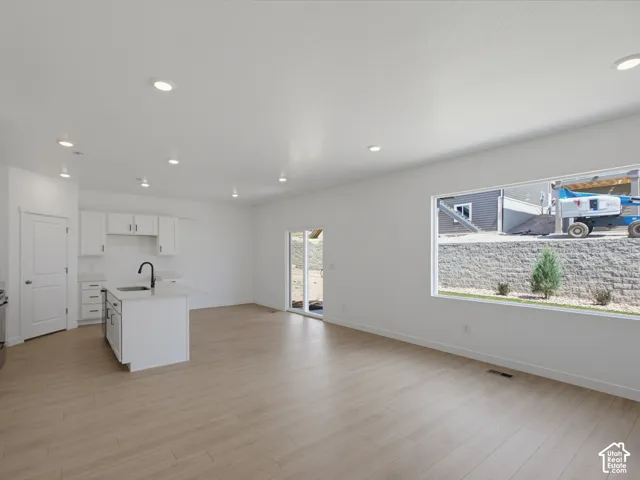 Open-concept interior featuring light wood-finish flooring, recessed lighting, white cabinetry, a center island with a matte black faucet, and expansive windows