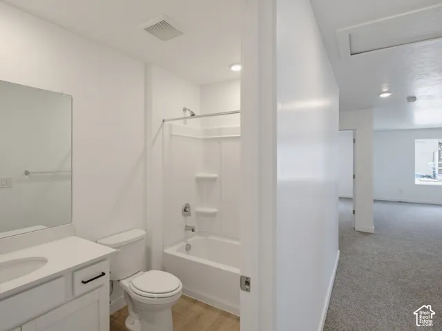 Bathroom featuring a vanity with a white countertop and rectangular sink, a combination shower and tub with white surround, and wood-finish flooring