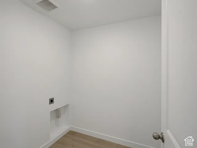 Enclosed utility area featuring wood-finish flooring, white walls, and a recessed plumbing connection box with a metal escutcheon plate
