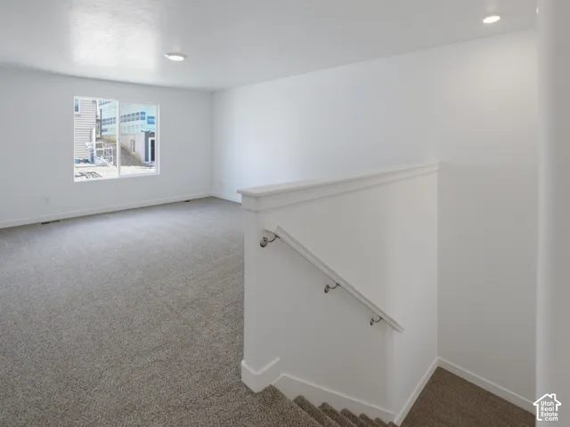 Neutral-toned wall-to-wall carpeting, recessed ceiling lighting, and a painted wood staircase railing