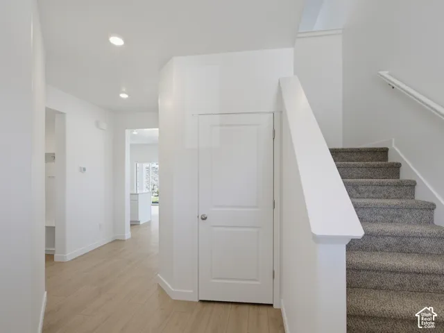 Interior hallway featuring wood-finish flooring, recessed lighting, a paneled interior door, and a carpeted staircase with a painted handrail