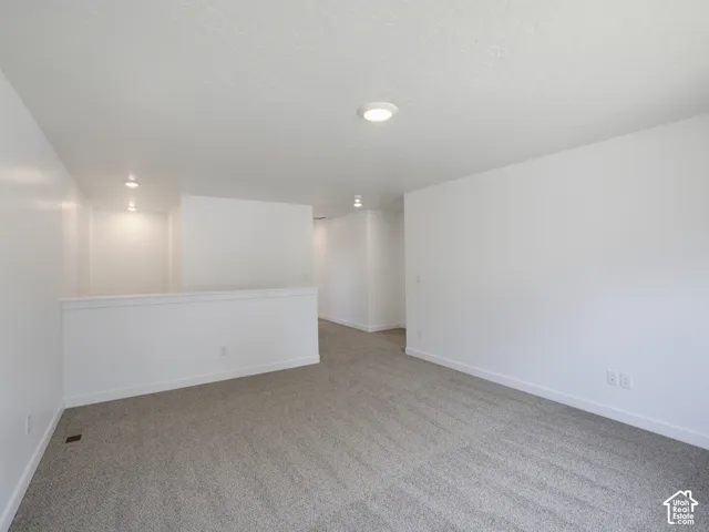 Neutral-toned carpeting, minimalist white walls, recessed ceiling lighting, and a painted half-wall partition
