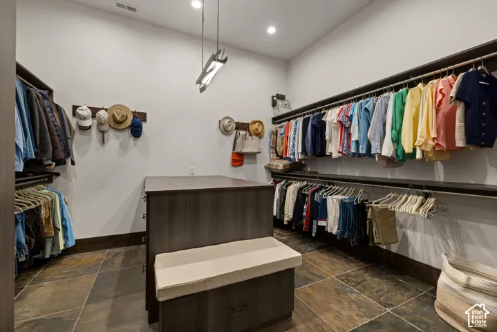 Walk-in dressing room featuring custom dark wood-finish cabinetry, tiered hanging rods, a central island with integrated storage, and multi-tone stone flooring