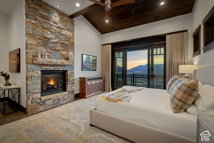 Floor-to-ceiling stone fireplace with a thick stone mantel, vaulted ceilings with dark wood planking, and sliding glass doors opening to a balcony with mountain scenery
