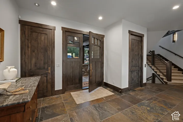 Entryway featuring dark-stained wood doors with glass inserts, stone tile flooring, and a staircase with wood railings and metal mesh paneling