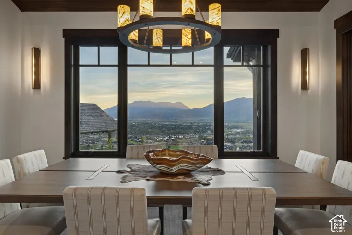 Large picture windows with dark wood trim, rustic circular chandelier, matching wall-mounted sconces, dark wood-finished ceiling accents, and mountain backdrop