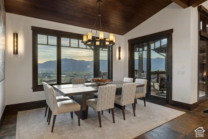 Vaulted ceiling with stained wood tongue-and-groove planking, oversized picture windows, mountain backdrop, multi-tone stone flooring, and wrought-iron style chandelier