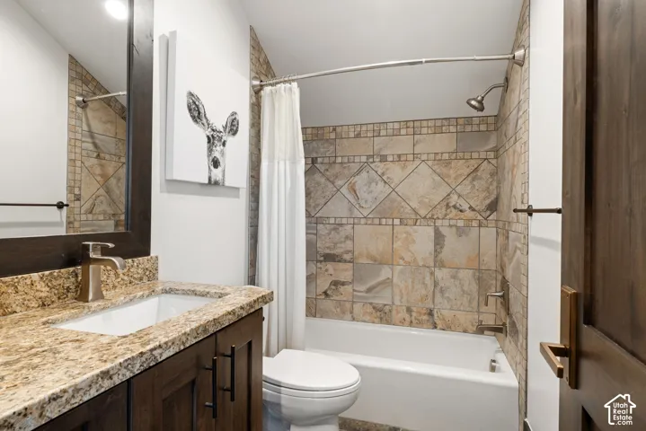 Bathroom featuring dark-stained wood cabinetry, stone-finish countertop, undermount sink, and tile-surround tub with metallic fixtures