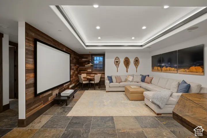 Media room featuring a tray ceiling with recessed lighting, large-format stone tile flooring, and a decorative wood-plank accent wall