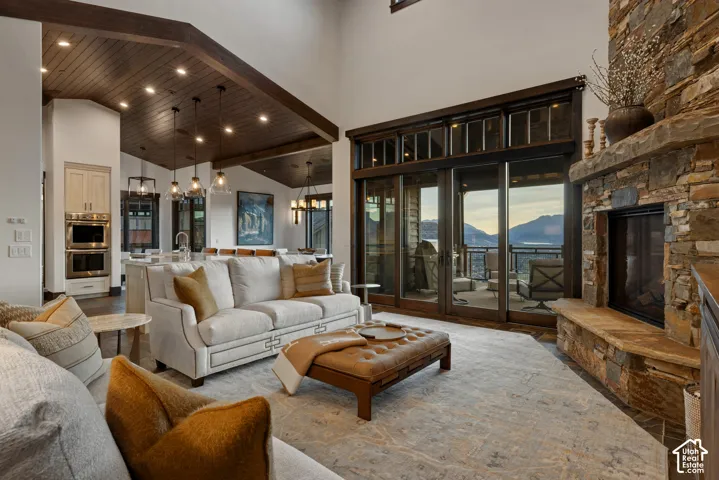 Vaulted ceilings with wood-plank detailing, floor-to-ceiling stone fireplace, multi-panel sliding glass doors, built-in double wall ovens, and recessed lighting