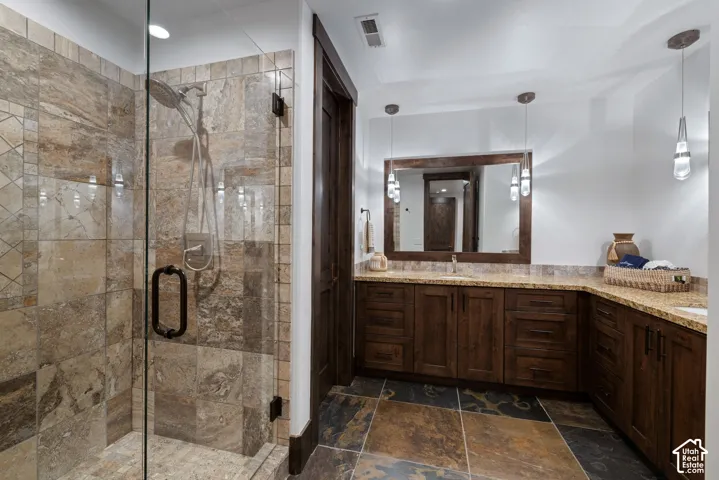 Walk-in shower with stone tile surround, custom dark wood cabinetry, natural stone countertops, dual drop-in sinks, and large-format multi-tone tile flooring