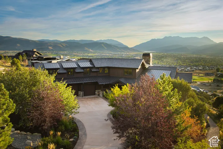 Multi-level exterior featuring dark wood siding, a metal roof, stone chimney, and a concrete driveway set against a mountain backdrop