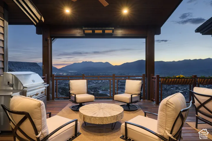 Covered outdoor deck featuring wood-finish decking, built-in stainless steel grill, recessed lighting, and mountain backdrop