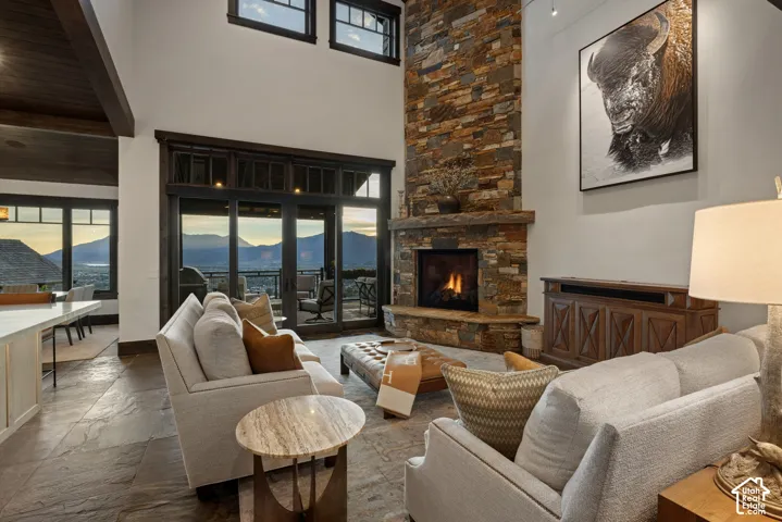 Double-height living area featuring a full-height stone masonry fireplace with a natural stone hearth, expansive multi-panel sliding glass doors, dark-stained timber ceiling beams, and stone flooring
