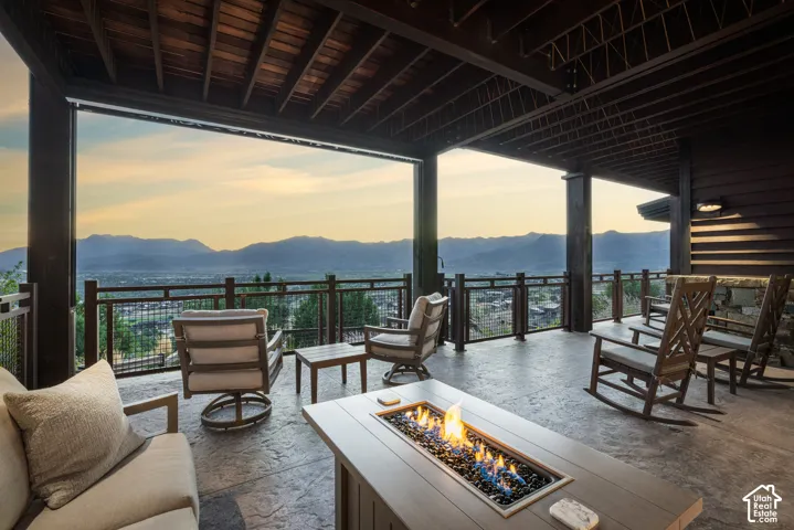 Covered outdoor terrace featuring a stamped concrete floor, timber-frame ceiling, integrated fire pit, and metal railing overlooking mountain scenery