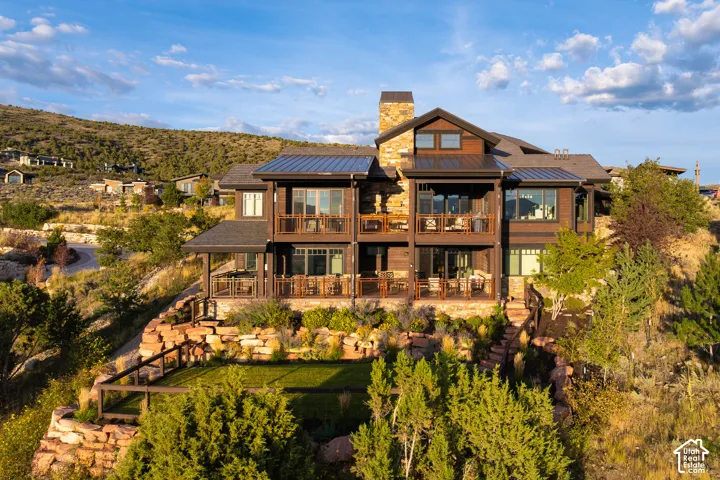 Multi-level exterior featuring wood siding, stone chimney, metal roof, tiered stone retaining walls, and tiered covered decks with railings
