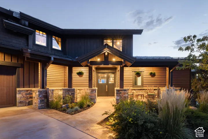 Exterior facade featuring dark wood-tone siding, stacked stone masonry, a covered porch entry, and a concrete walkway