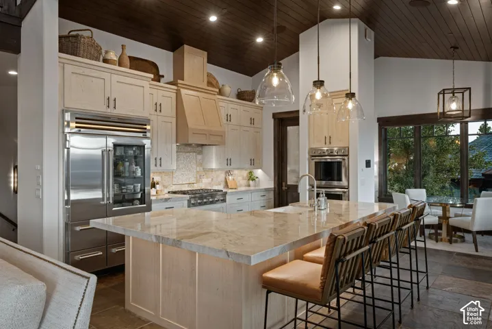 Kitchen featuring light wood cabinetry, stone countertops, stainless steel appliances, dark wood-plank ceiling, and glass pendant lighting
