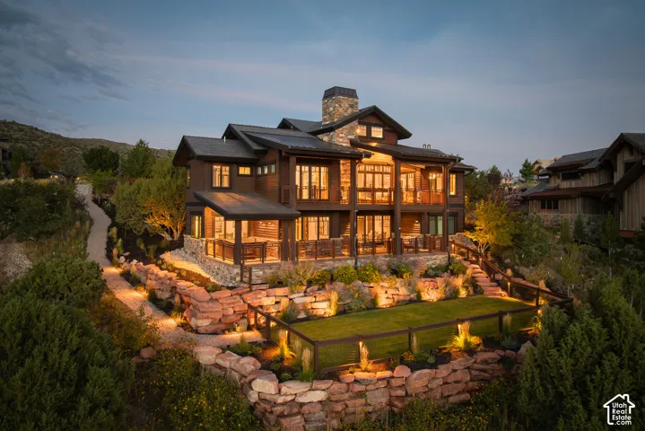 Multi-level mountain residence featuring tiered natural stone retaining walls, wrap-around covered decks, stone-clad chimney, and custom landscaping with an enclosed lawn area