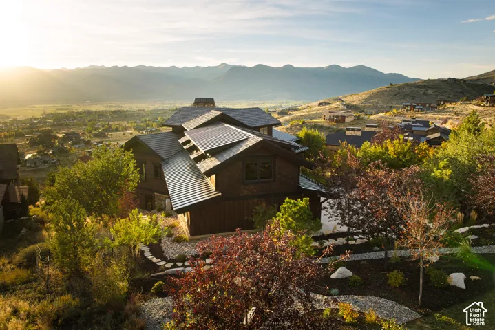 Multi-level exterior featuring dark wood siding, a metal roof, solar panels, and stone landscaping accents, set against a backdrop of mountain peaks