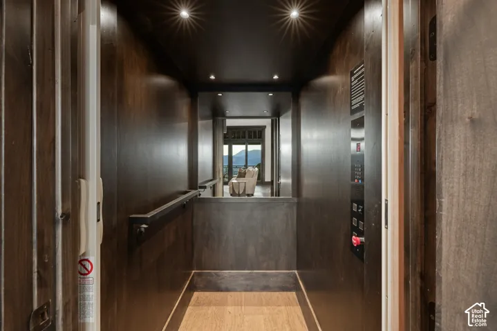 Interior elevator featuring dark wood-finished paneling, recessed lighting, a horizontal handrail, and light-toned flooring