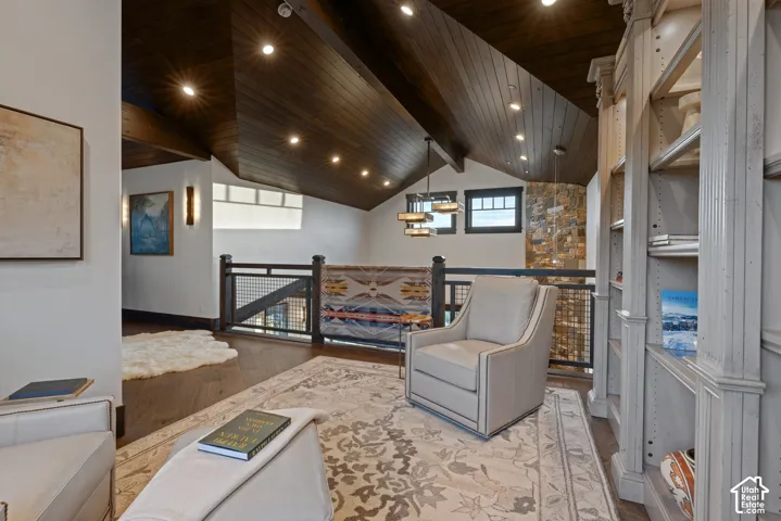 Vaulted ceiling with stained wood tongue-and-groove paneling, exposed structural beams, floor-to-ceiling natural stone masonry, integrated recessed lighting, and custom built-in floor-to-ceiling cabinetry