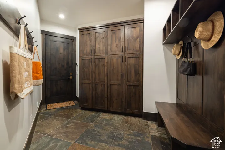 Mudroom featuring built-in floor-to-ceiling cabinetry, dark wood-finish bench with overhead cubbies, natural stone tile flooring, and matching wood-trimmed door