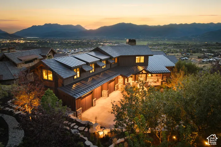 Mountain residence featuring metal roofing, stone masonry accents, wood siding, and an attached multi-car garage, set against a prominent mountain backdrop