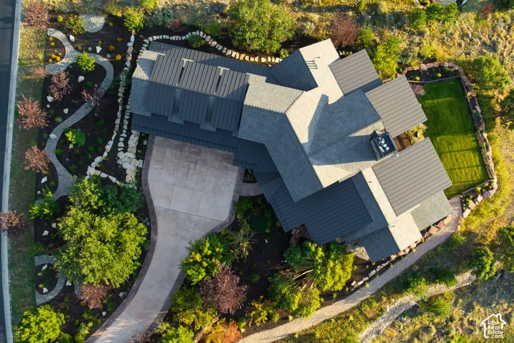 Aerial perspective featuring a metal roof, concrete driveway, stone-bordered landscaping, and a manicured lawn