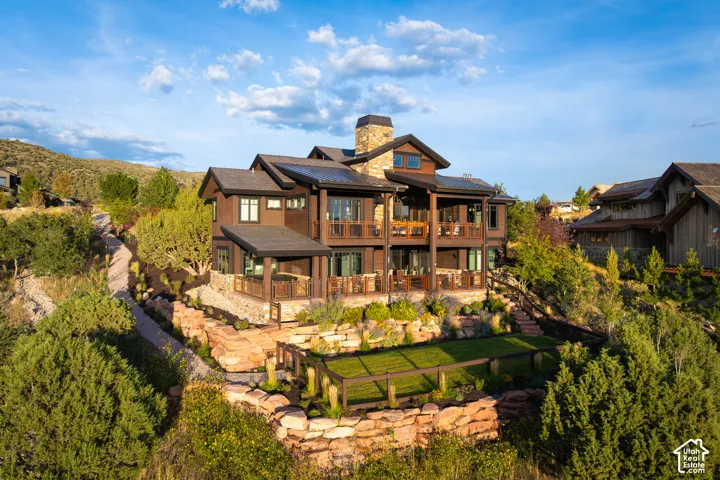 Custom residence featuring multi-level covered balconies, tiered natural stone retaining walls, wood-finish siding, and a stone-clad chimney